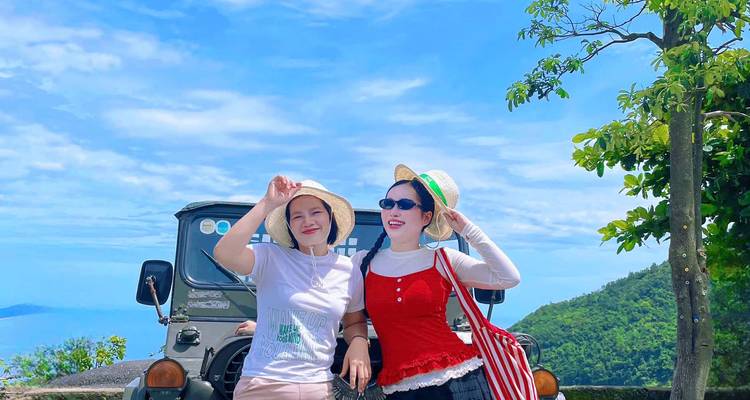 Two women with hats posing in front of a jeep with a scenic mountain view.