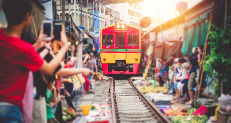 Toeristen die foto's maken van een trein die door een drukke markt rijdt.