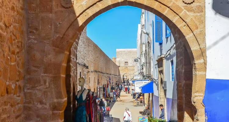 Busy street with shops and people viewed through a stone archway.