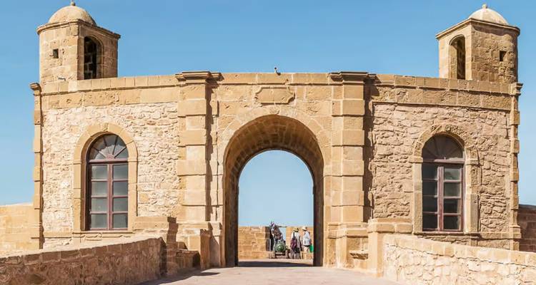 Stone archway with two towers viewed from a bridge.