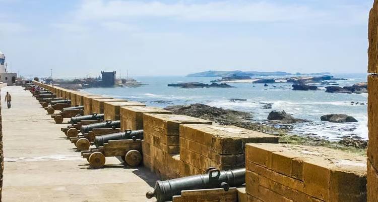 Historical wall with cannons along a coastal fortification.