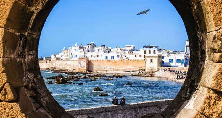 Seaside view of a city through an arch with people sitting in the foreground.