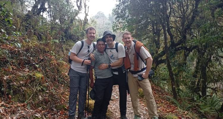 Drie trekkers omhelzen hun Nepalese drager op een met bladeren bezaaid junglepad.