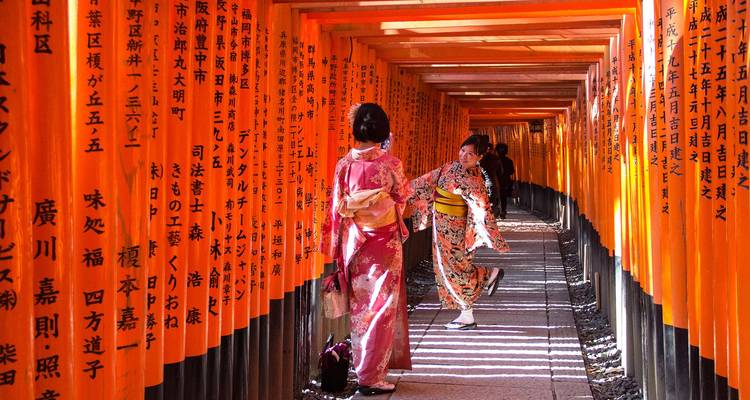 Two women in colorful kimonos pose among endless rows of orange torii gates with Japanese calligraphy
