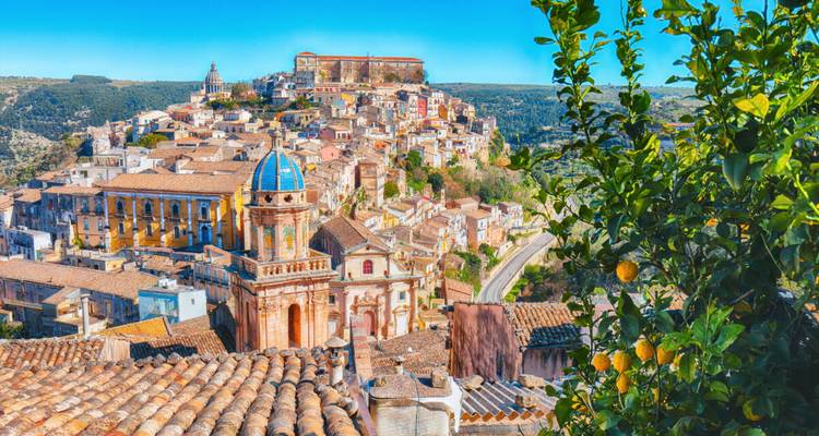 Lebhaftes Panorama der barocken Dächer von Ragusa Ibla, umrahmt von Zitrusblättern unter einem lebendigen blauen Himmel