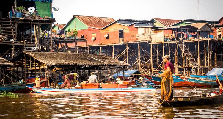 Village flottant avec maisons colorées sur pilotis et bateaux sur une voie navigable.
