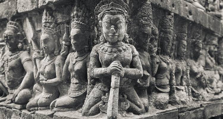 Sculptures en pierre de divinités sur un mur de temple, dans des tons sépia.