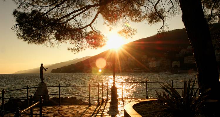 Coucher de soleil sur la mer avec une statue et une balustrade en silhouette.