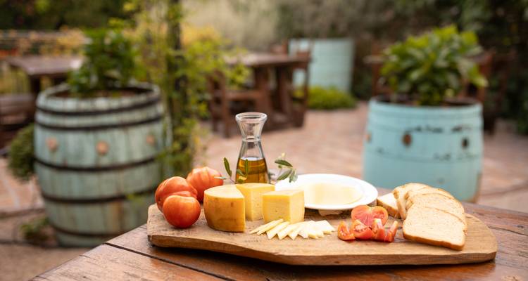 Plateau avec fromage, tomates, pain et huile d'olive en extérieur.