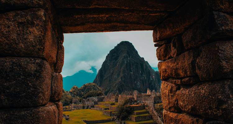 Vue à travers une porte en pierre du Machu Picchu avec des montagnes en arrière-plan.