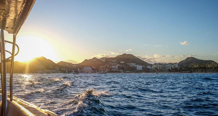 Vista de un pueblo costero desde el mar con el sol poniéndose detrás de las colinas.