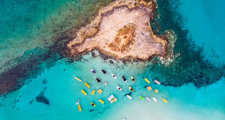 Vista aérea de aguas turquesas con barcos cerca de una isla rocosa.