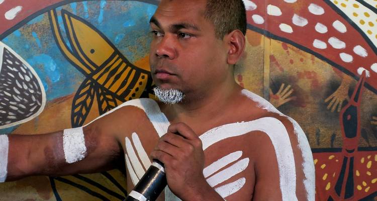 Inheemse persoon die spreekt voor een muurschildering.