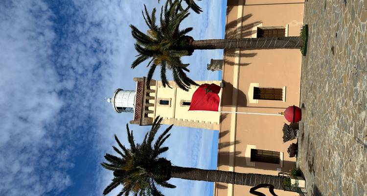 Phare avec un drapeau et des palmiers au premier plan.
