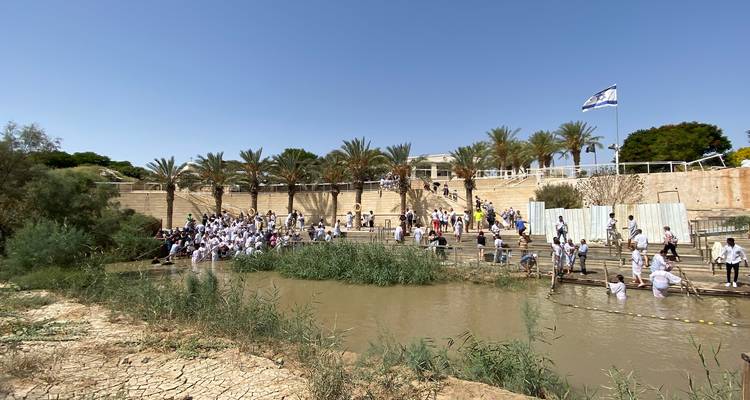 Groupe de personnes rassemblées près d'une rivière avec des drapeaux au-dessus.