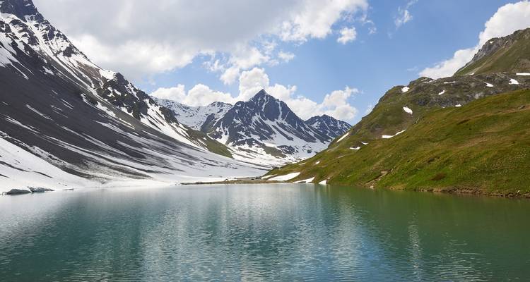 Lac de montagne avec des sommets enneigés au loin.