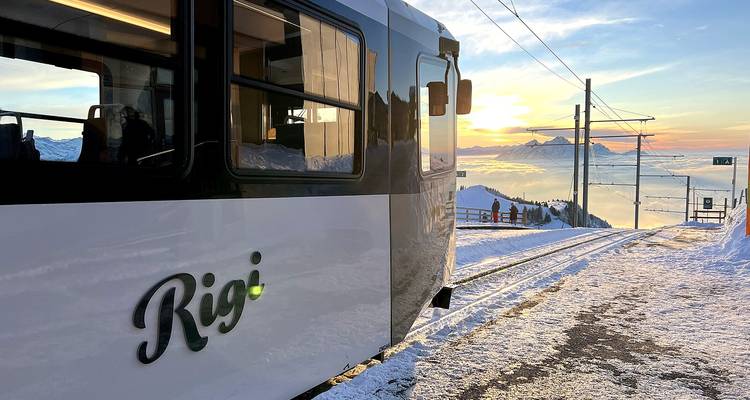 Train sur des rails enneigés avec un coucher de soleil en arrière-plan.