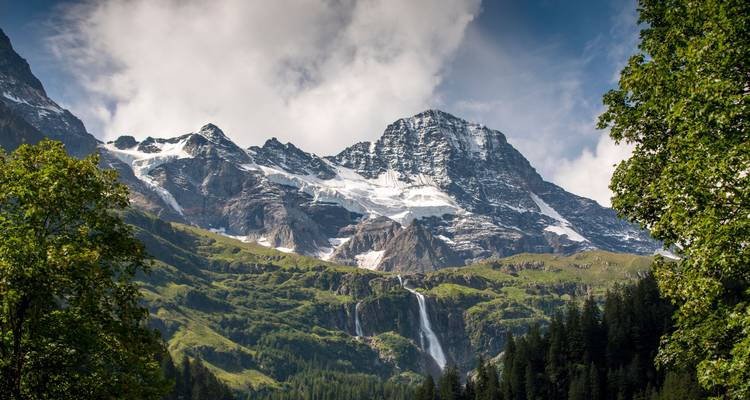 Paysage de montagne avec une cascade et des sommets enneigés.