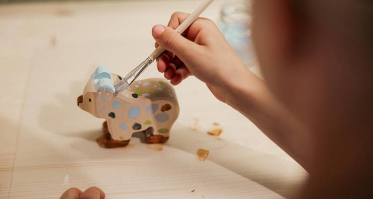 Person painting a small wooden animal figure.