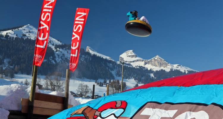 Person in an inflatable tube in mid-air against a snowy mountain backdrop.
