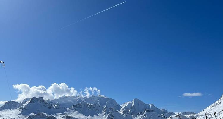 Sommets de montagnes enneigés avec une traînée de condensation dans le ciel.