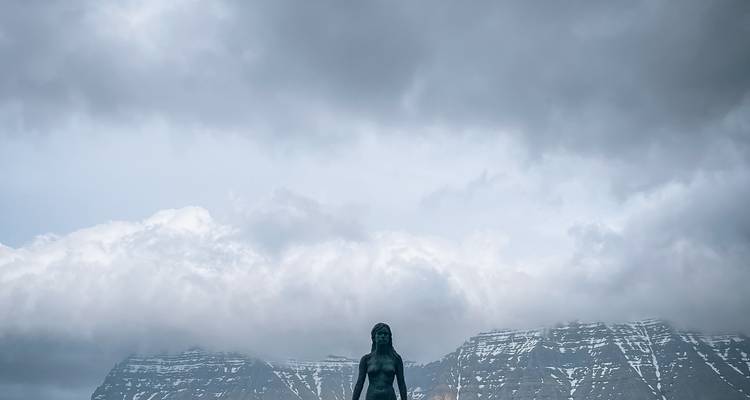 Statue avec toile de fond montagneuse et nuages dramatiques.