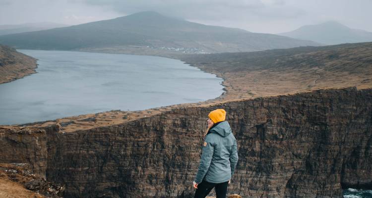 Personne debout sur une falaise surplombant un fjord.