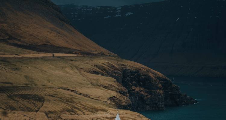 Grande montagne avec des pentes brunes et un voilier au loin.
