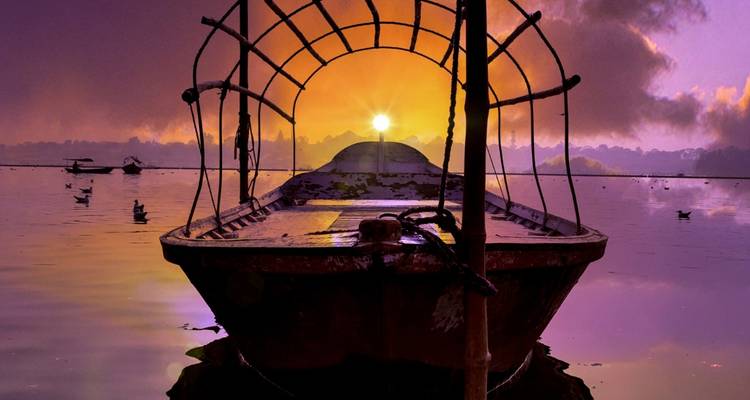 A serene boat at sunset on a lake with beautiful lighting.