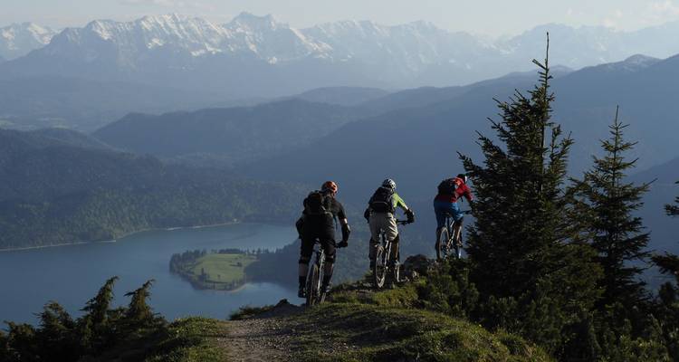 Radfahrer auf einem Weg mit Blick auf Berge und einen See.