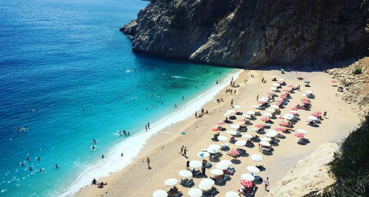 Sandstrand mit Sonnenschirmen und Menschen, die das Wasser genießen.