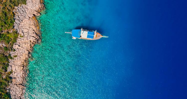 Luftaufnahme einer Yacht auf tiefblauem Meer neben felsiger Küstenlinie.