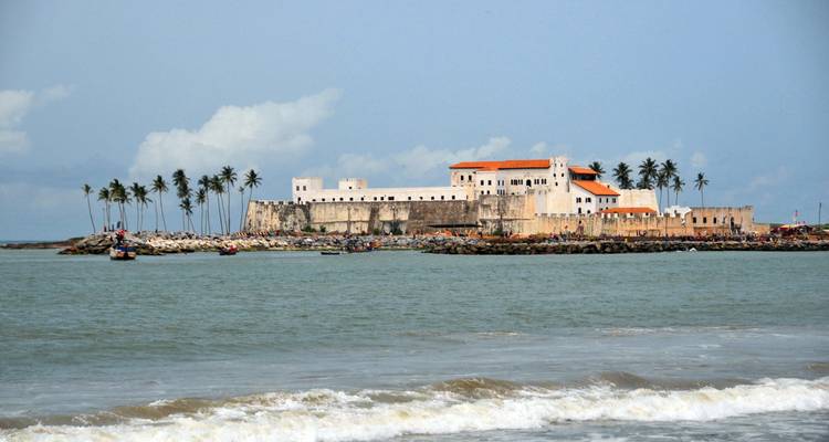 Château de Cape Coast sur une côte rocheuse avec des palmiers.