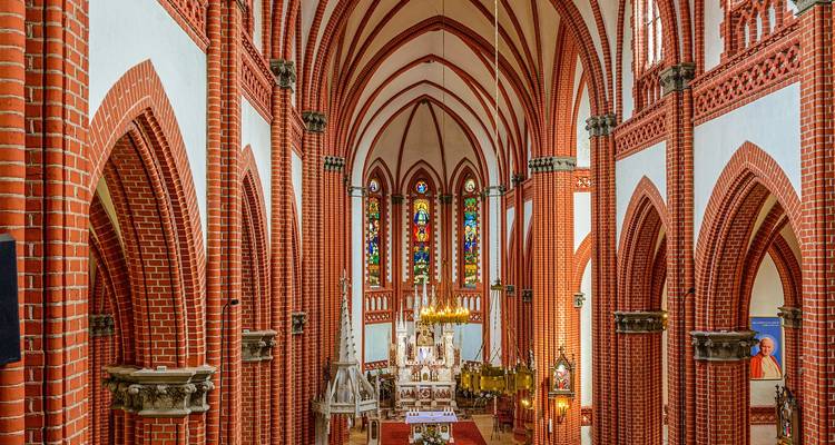 Intérieur d'une église gothique avec des arcs en brique rouge et des vitraux.