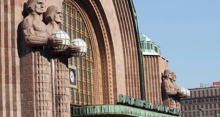 Façade de gare de style Art déco avec des statues tenant des globes.