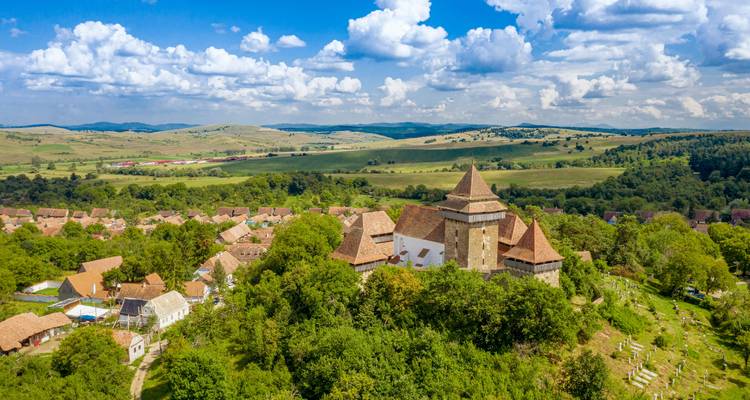 Vue aérienne d'une église fortifiée historique entourée de champs verts.