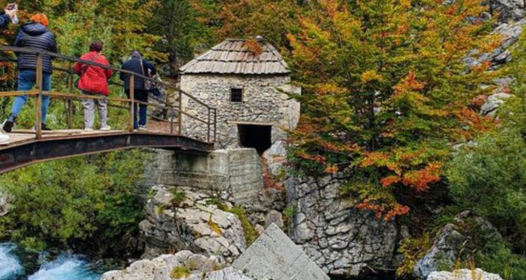 Turistas caminando a través de un puente cerca de una estructura de piedra.