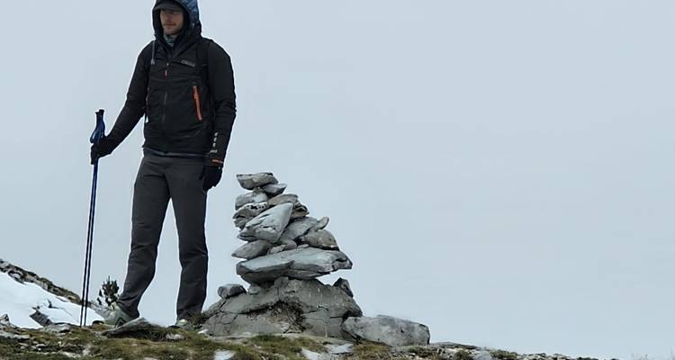 Excursionista de pie junto a un mojón de piedra.