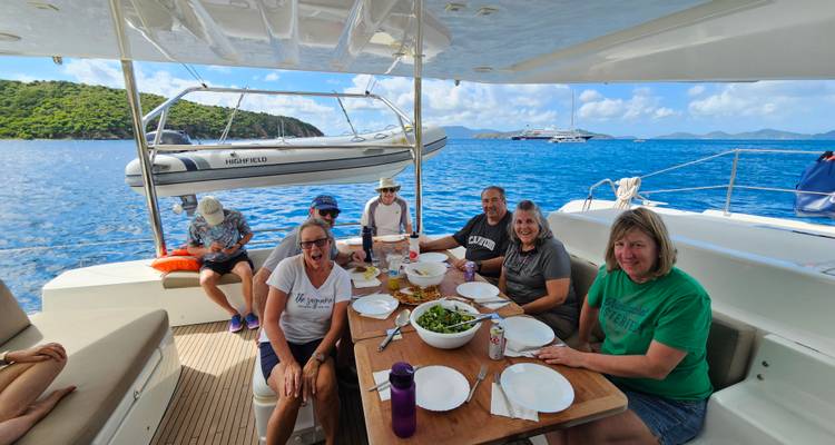 Group of people dining on a boat with islands in background.