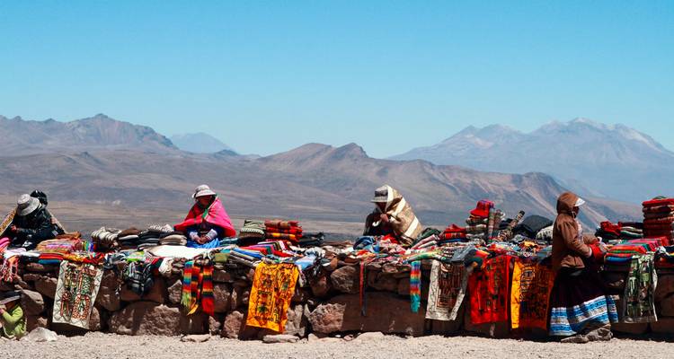 Local people selling colorful textiles against mountain backdrop.