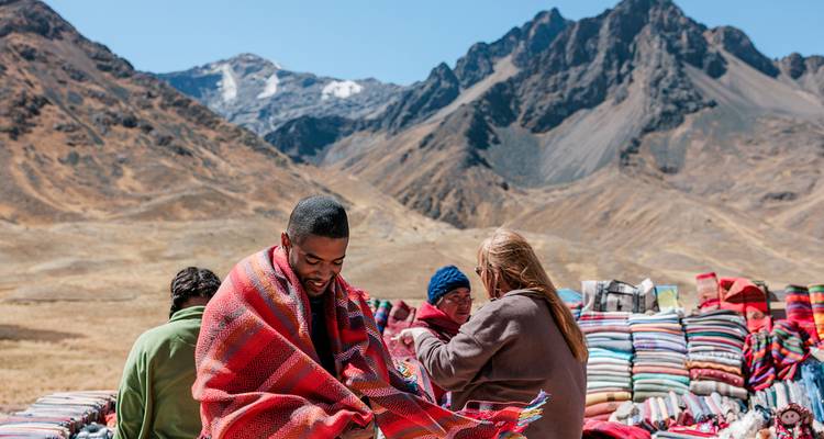 People interacting with colorful textiles in a mountainous setting.