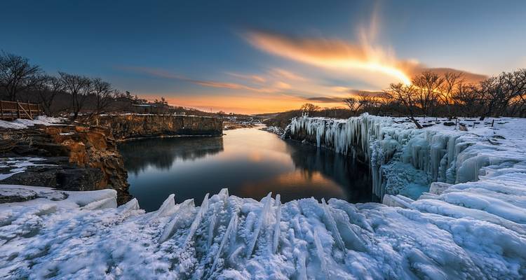 Paysage gelé avec une rivière glacée et un ciel dramatique.