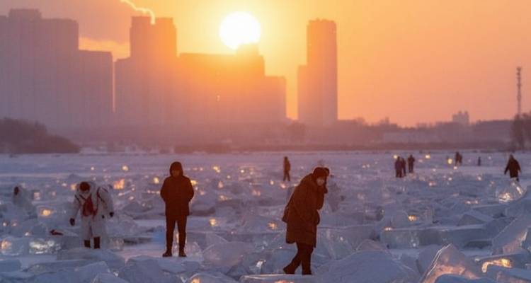 Des gens marchant sur la glace sous un soleil couchant à Harbin.