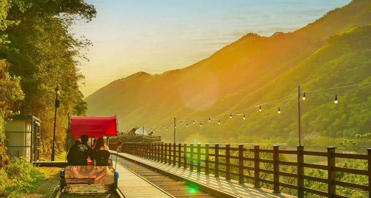 Wagon de chemin de fer sur des rails avec coucher de soleil et montagnes.