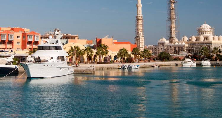 Scène ensoleillée de marina avec yachts, promenade bordée de palmiers et mosquée imposante à Hurghada.