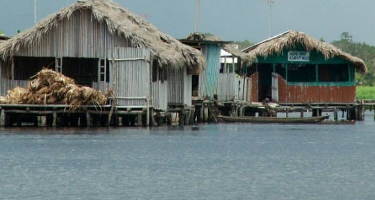 Maisons sur pilotis au-dessus de l'eau avec un bateau devant.