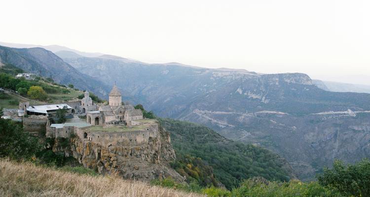 Un monasterio antiguo situado en un acantilado con montañas al fondo.