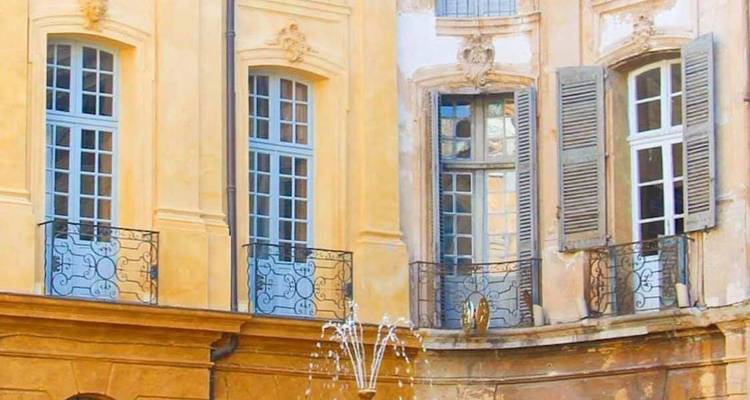 Façade élégante de bâtiment avec balcons en fer forgé et une fontaine.