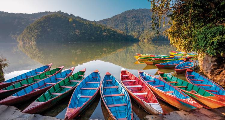 Kleurrijke boten op een meer met weelderige heuvels op de achtergrond.