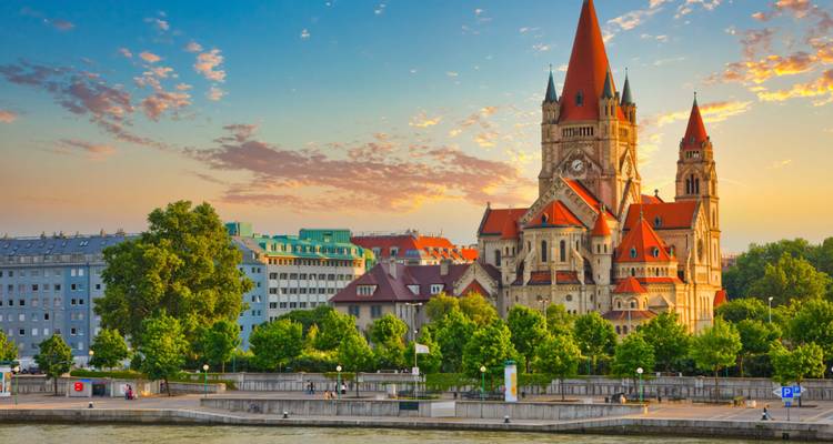Church with red roofs and a river in front, with a sunset sky.